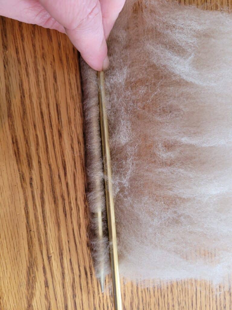 rolling thin bed of wool around two pinched knitting needles to make a faux rolag