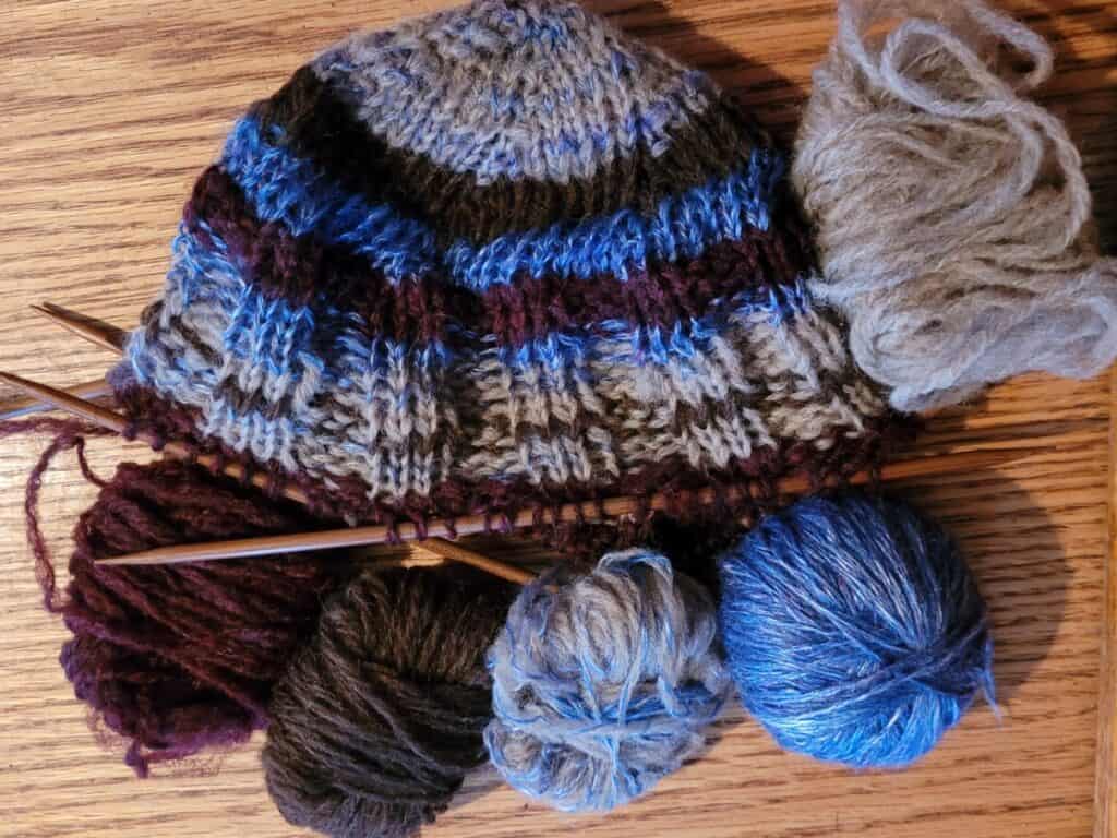 top down hat on double pointed needles being knitted from extra balls of yarn of various fibers